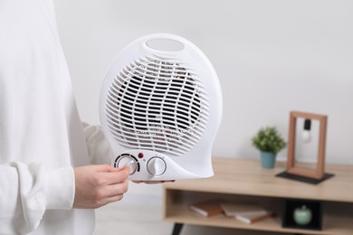 Woman turning on electric fan heater at home, closeup. Space for text