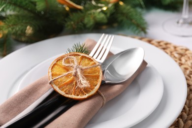 Photo of Festive place setting with beautiful dishware, fabric napkin and dried orange slice for Christmas dinner on white table, closeup