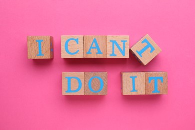Photo of Motivation concept. Changing phrase from I Can't Do It into I Can Do It by removing wooden cube with letter T on pink background, top view