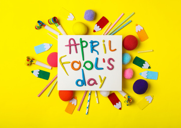 Paper note with phrase APRIL FOOL'S DAY and decor on yellow background, flat lay
