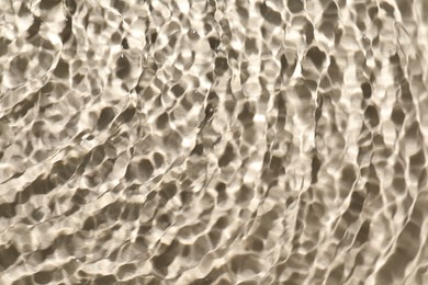 Rippled surface of clear water on beige background, top view