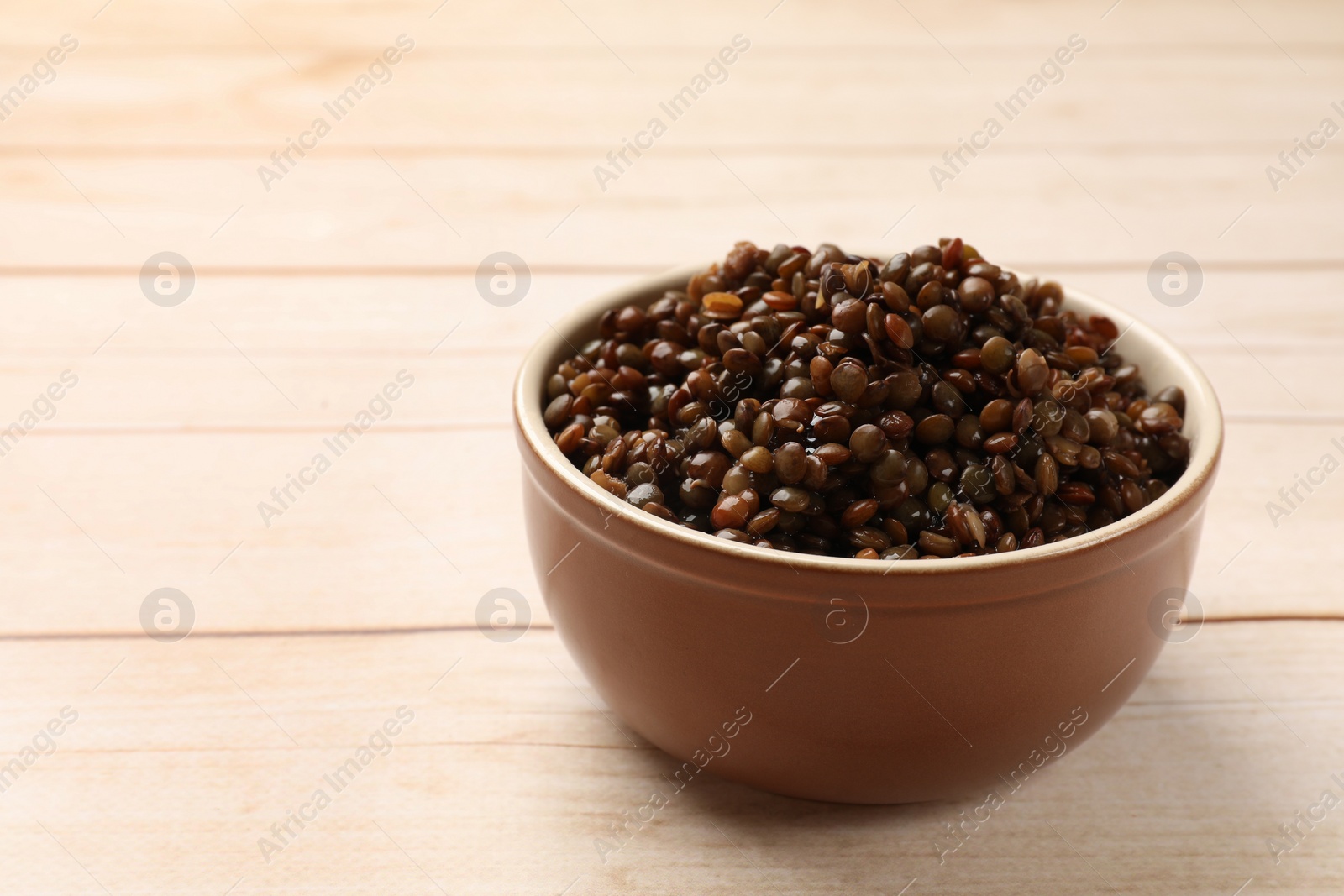 Photo of Delicious lentils in bowl on wooden table, closeup. Space for text