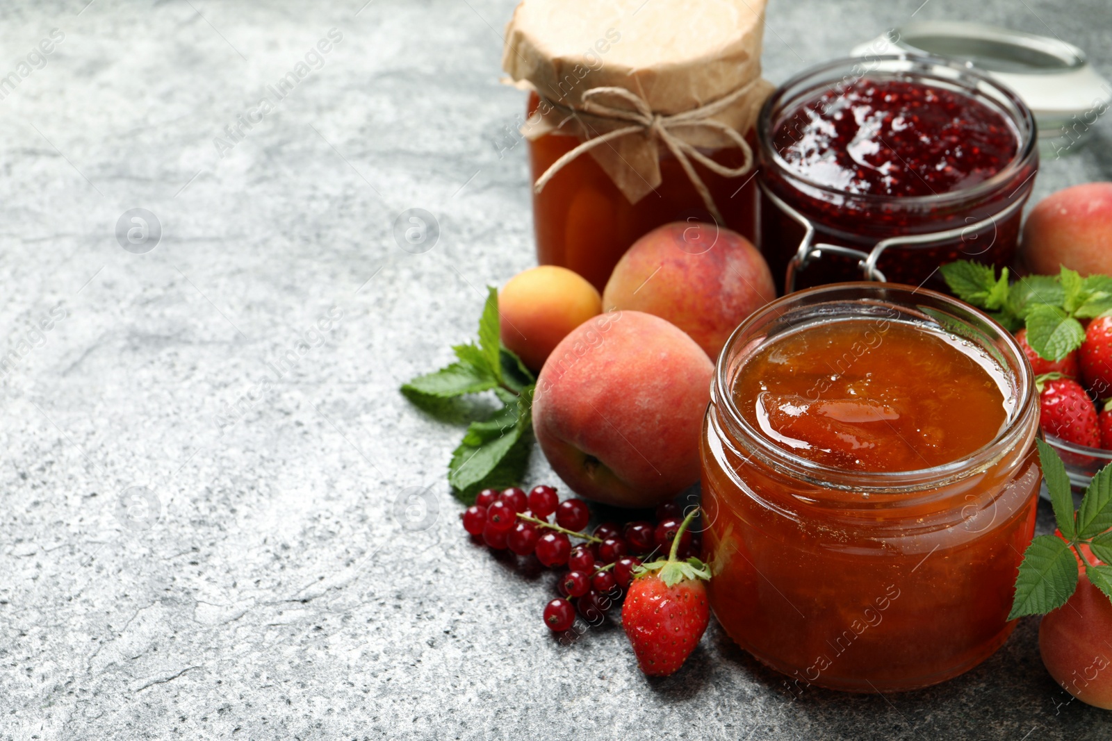 Photo of Jars with different jams and fresh fruits on grey table. Space for text