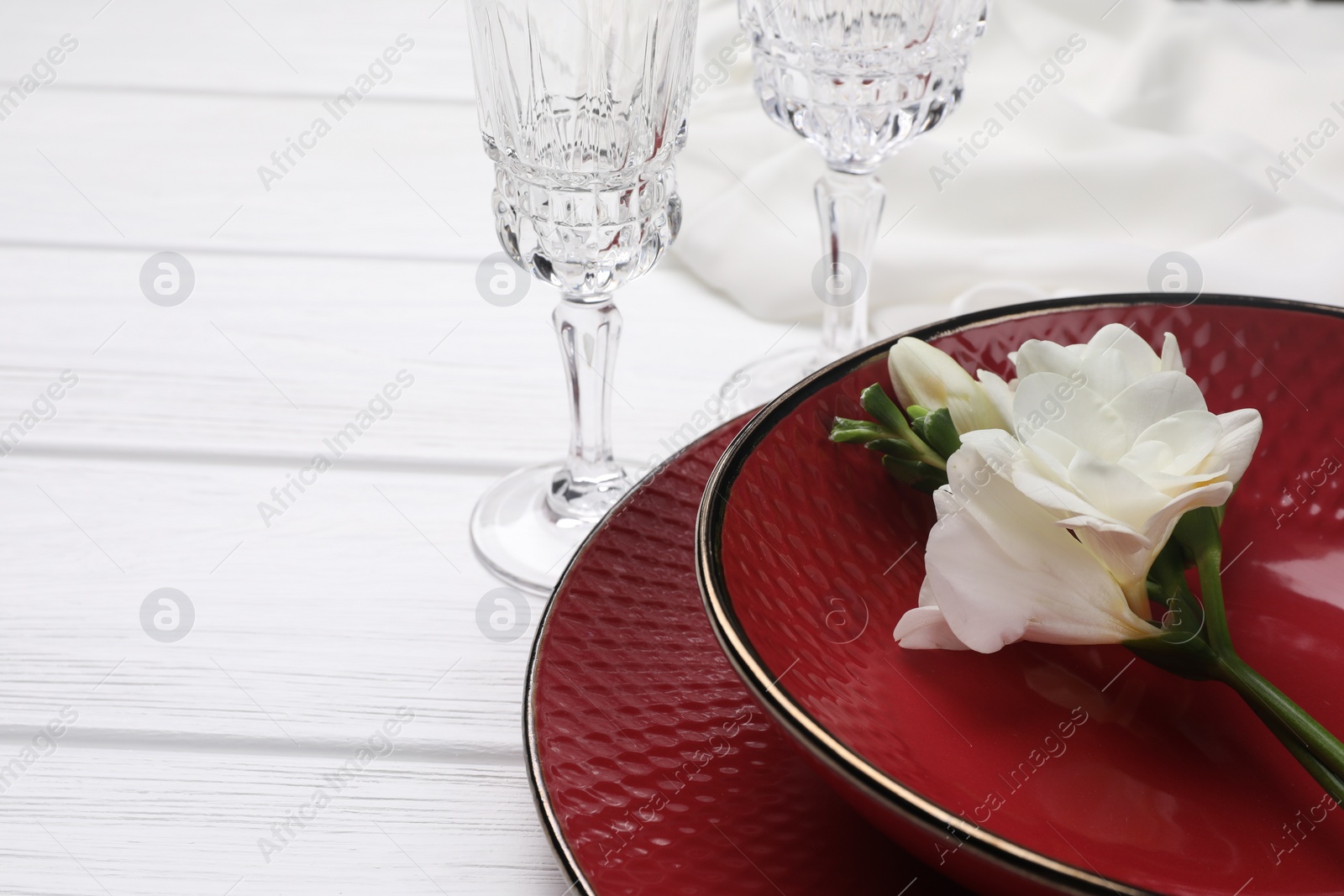 Photo of Dishes with flower and glasses on white wooden table, closeup. Space for text