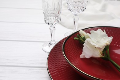 Dishes with flower and glasses on white wooden table, closeup. Space for text