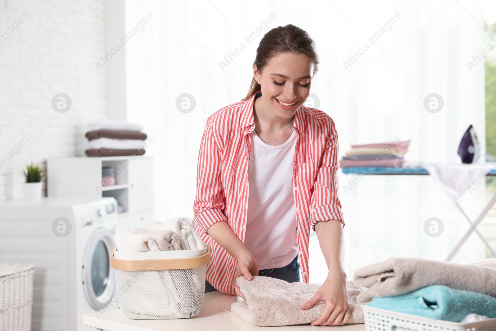 Photo of Happy woman folding clean towel at table indoors. Laundry day