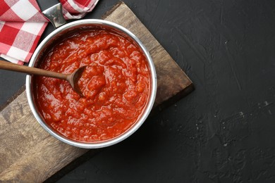 Photo of Homemade tomato sauce and spoon in pot on dark textured table, top view. Space for text