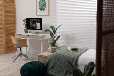 Photo of Comfortable bed, desk with computer and potted houseplants in stylish bedroom. Interior design