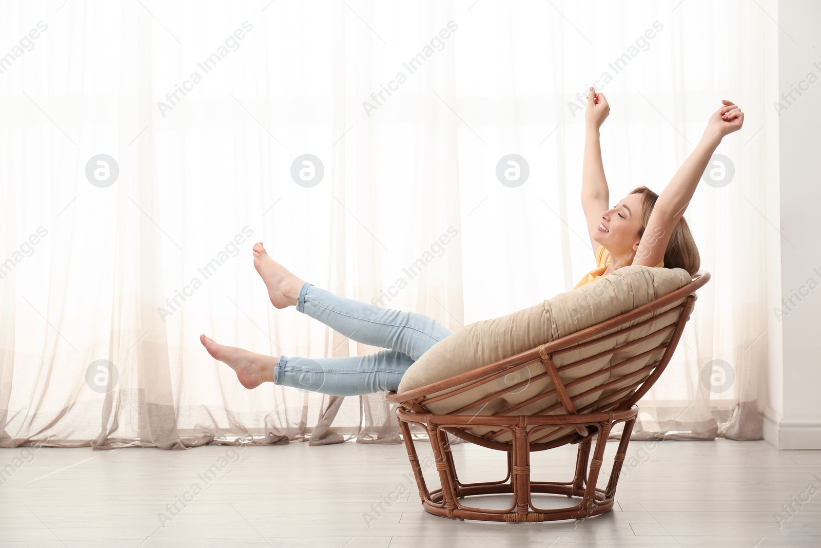 Photo of Beautiful young woman stretching in papasan chair at home, space for text