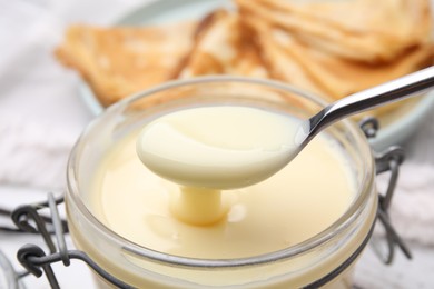 Photo of Taking tasty condensed milk from jar with spoon at table, closeup