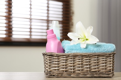 Clean towels with lily and detergents in basket on table indoors. Space for text