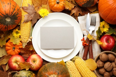 Table setting surrounded by autumn vegetables, leaves and flowers on wooden background, flat lay. Thanksgiving Day celebration