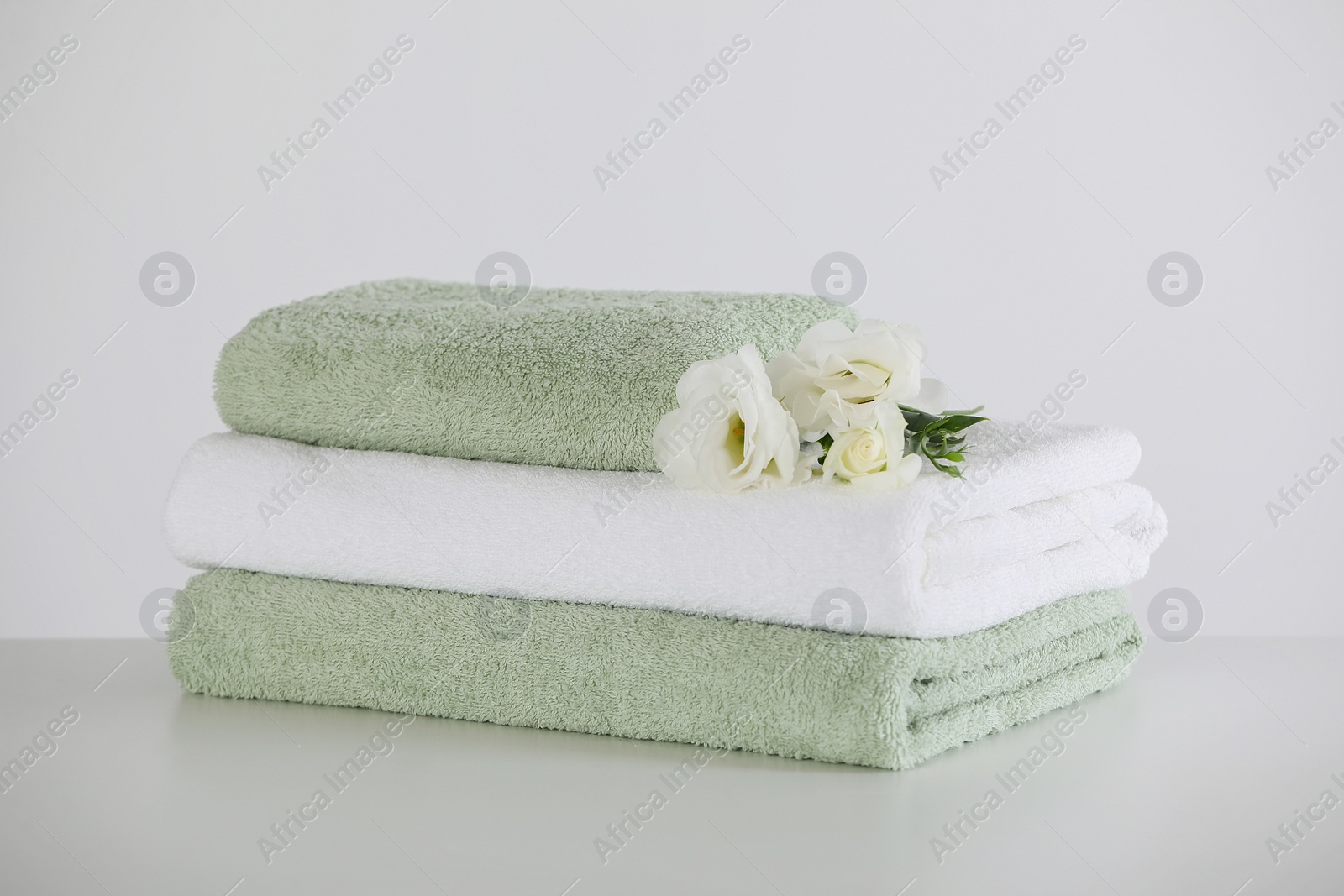 Photo of Soft folded towels with eustoma flowers on white table