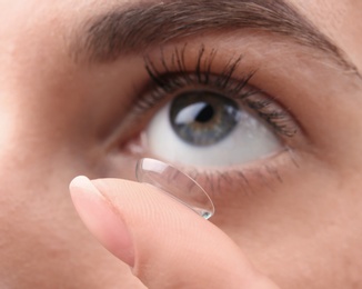 Photo of Young woman putting contact lens in her eye, closeup