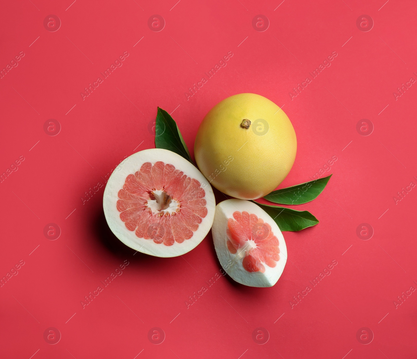 Photo of Fresh cut and whole pomelo fruits with leaves on red background, flat lay