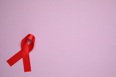 Photo of Top view of red ribbon on violet background, space for text. AIDS disease awareness