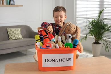 Photo of Cute little boy putting toy into donation box at home