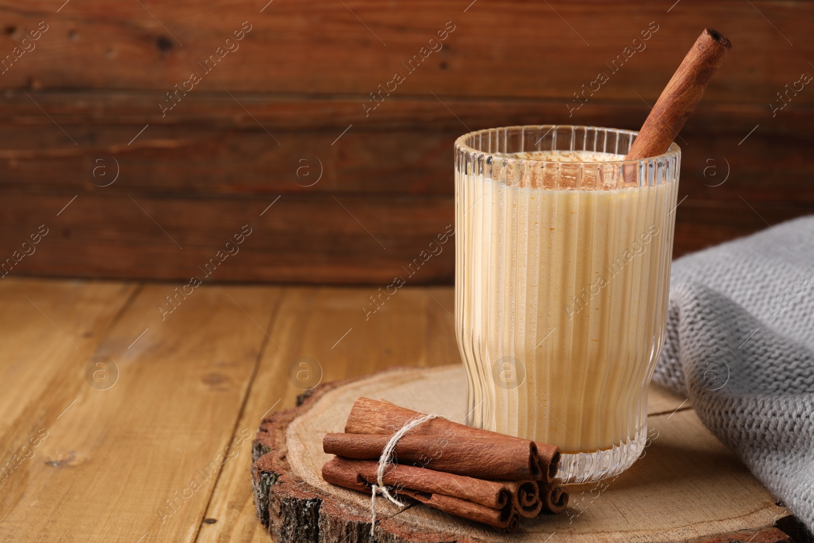 Photo of Glass of delicious eggnog with cinnamon on wooden table, space for text