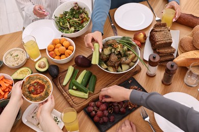 Photo of Friends eating vegetarian food at wooden table indoors, closeup