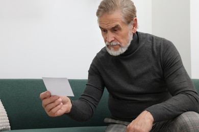 Photo of Upset senior man holding photo on sofa at home. Loneliness concept