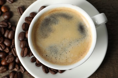 Photo of Cup of aromatic coffee and beans on wooden table, top view