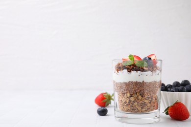 Photo of Tasty granola with berries, yogurt and chia seeds in glass on white tiled table, space for text