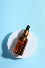 Bottle of cosmetic oil on light blue background, top view