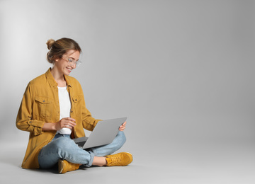 Young woman with laptop on grey background. Space for text