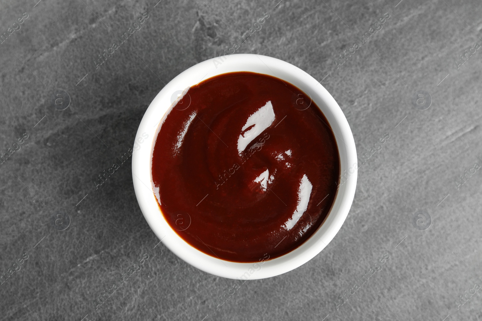 Photo of Barbecue sauce in bowl on grey background, top view