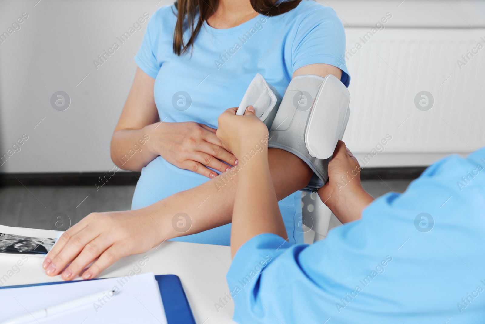 Photo of Doctor measuring blood pressure of pregnant woman in hospital, closeup