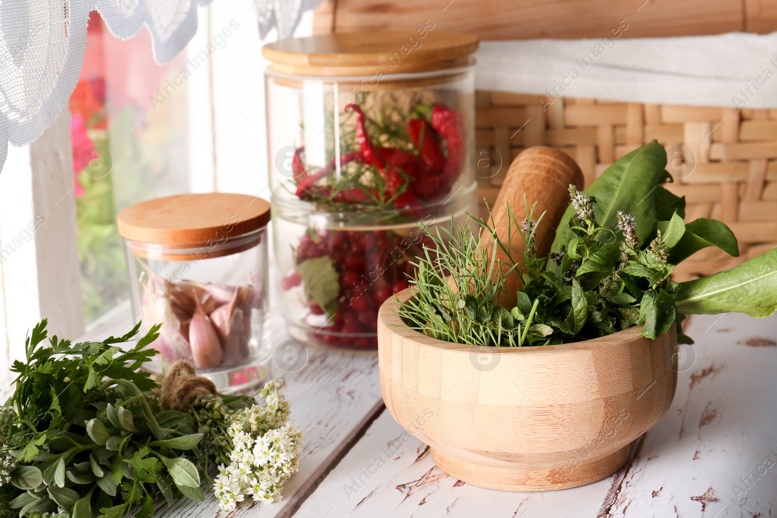 Photo of Mortar with pestle and fresh green herbs on white wooden table near window. Space for text