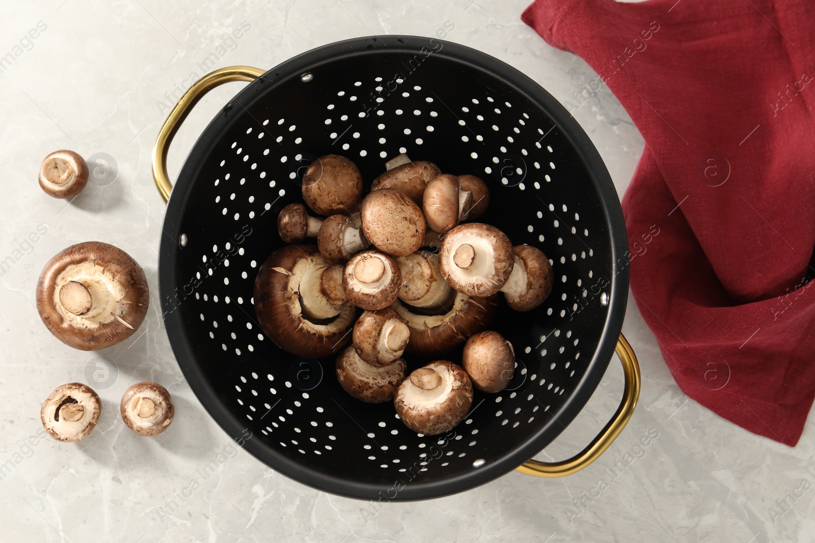 Photo of Raw mushrooms in black colander on marble table, flat lay