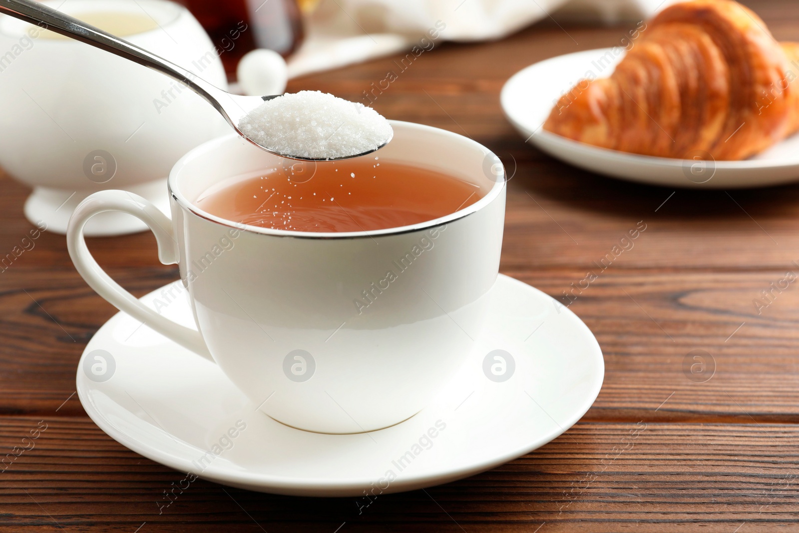 Photo of Adding sugar into cup of tea at wooden table, closeup