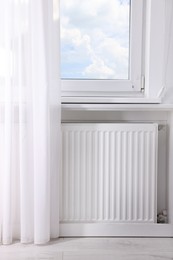 Photo of Modern radiator on wall under window indoors. Central heating system