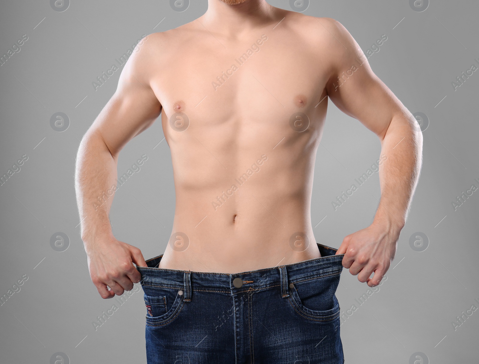 Photo of Young man with slim body in old big size jeans on grey background, closeup