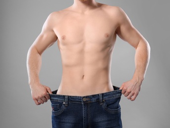 Young man with slim body in old big size jeans on grey background, closeup