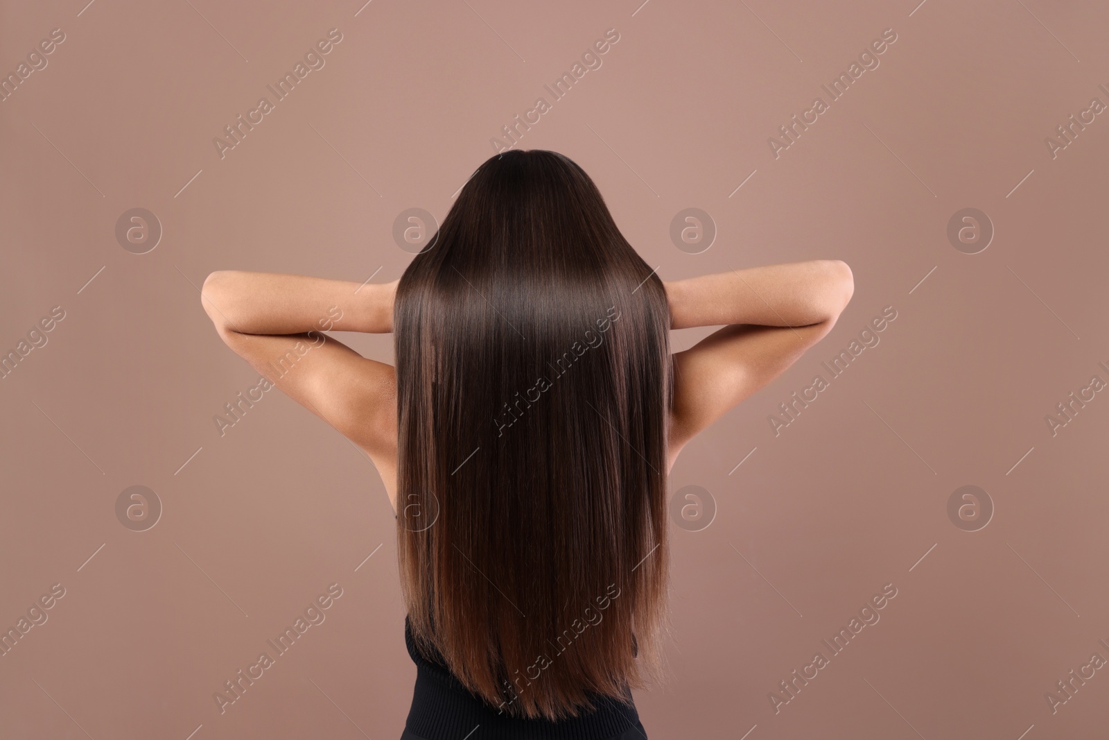 Photo of Hair styling. Woman with straight long hair on pale brown background, back view