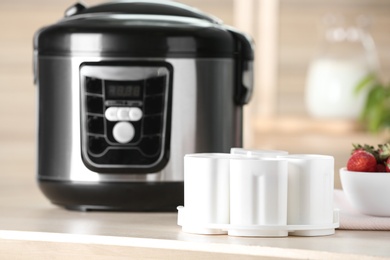 Modern multi cooker with cups for homemade yogurt on table in kitchen