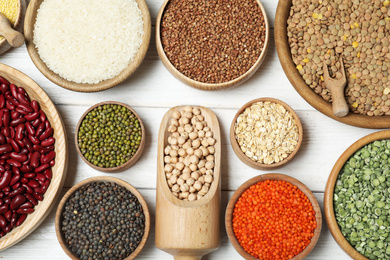 Photo of Different types of legumes and cereals on white wooden table, flat lay. Organic grains