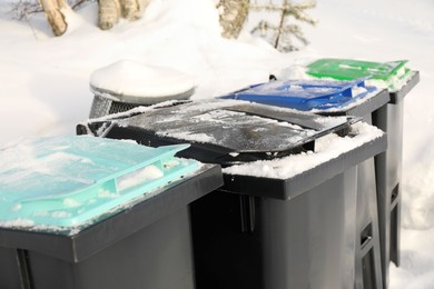 Photo of Many black recycling bins on snow outdoors, closeup. Winter season