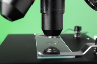 Photo of Modern medical microscope with glass slide on green background, closeup