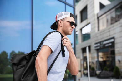 Photo of Handsome young man with stylish sunglasses and backpack near building outdoors