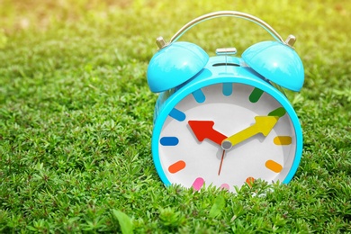 Alarm clock on green plants, outdoors. Time change concept
