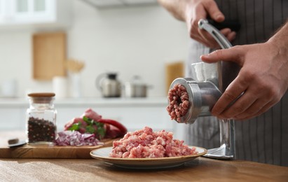 Photo of Man using hand meat grinder in kitchen, closeup