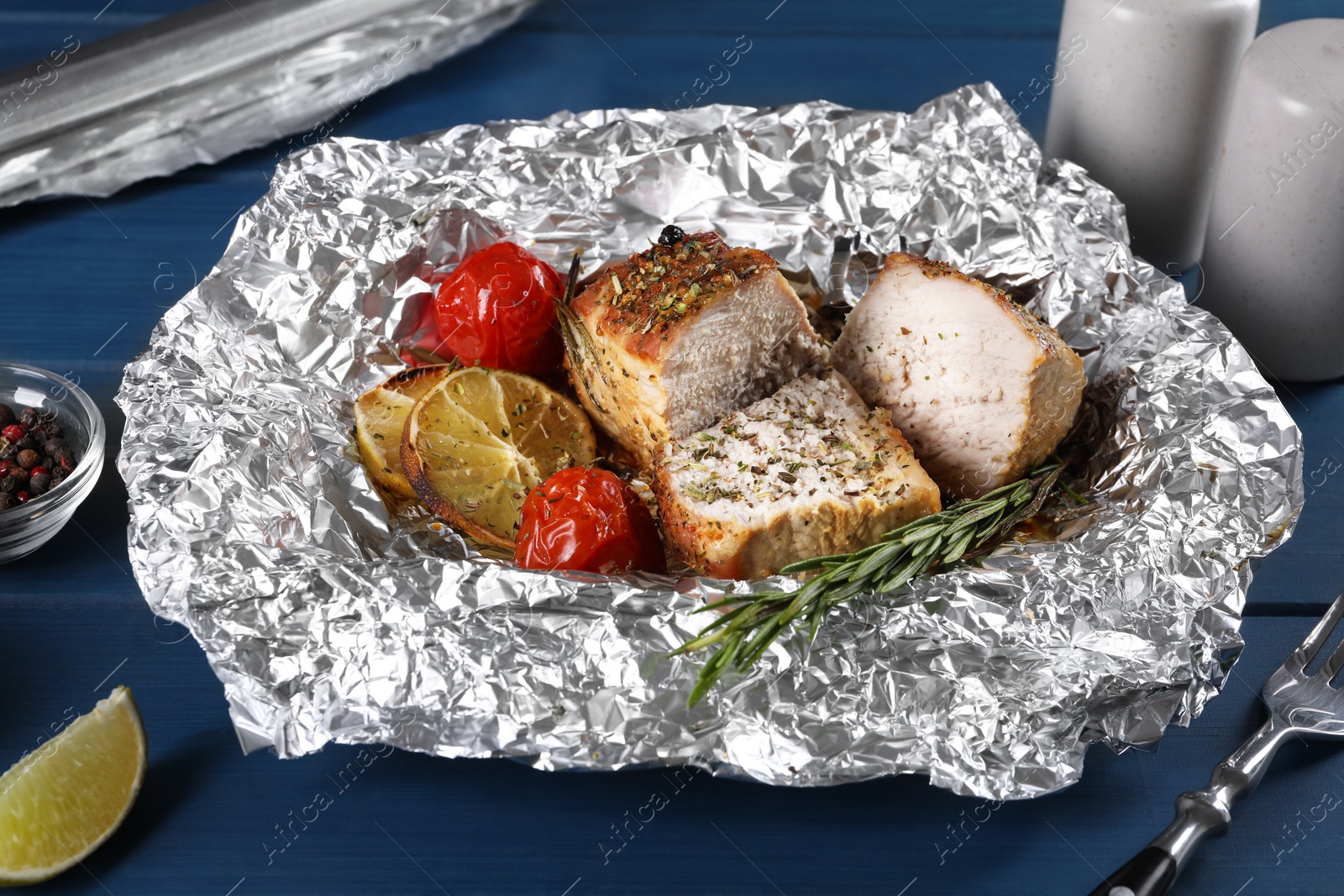 Photo of Pieces of delicious meat baked in foil with tomatoes on blue wooden table