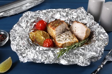 Pieces of delicious meat baked in foil with tomatoes on blue wooden table