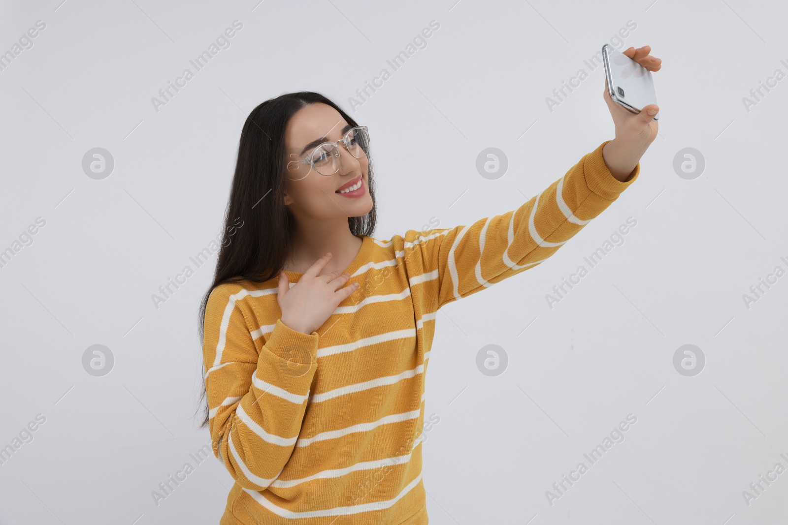 Photo of Smiling young woman taking selfie with smartphone on white background