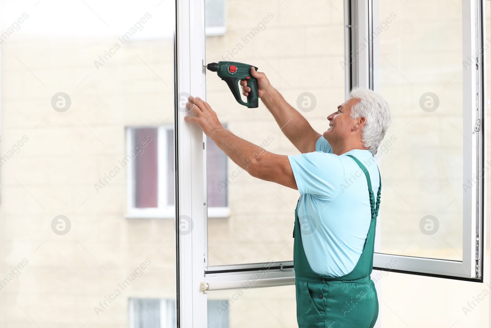 Photo of Mature construction worker repairing plastic window with electric screwdriver indoors