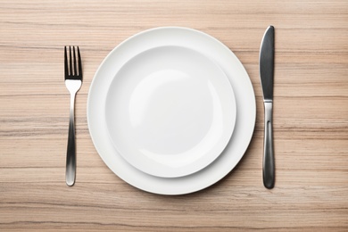 Photo of Stylish ceramic plates and cutlery on wooden background, flat lay