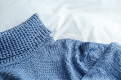 Photo of Stylish knitted sweater on white fabric, closeup